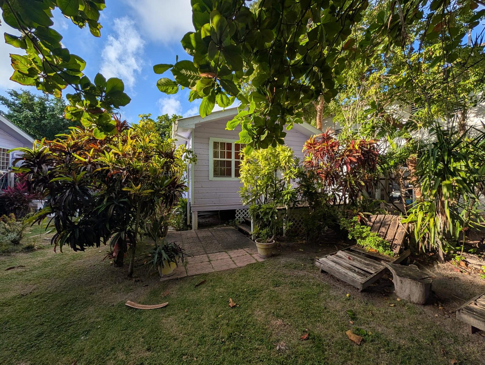 Caye Garden Casita exterior — gray clapboard cottage with red tropical flowers and blue sky